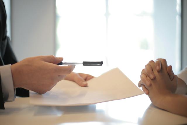 One person handing a contract to another over a table.
