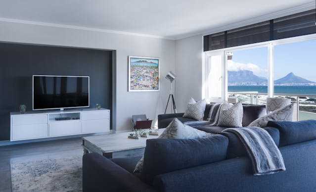 A modern interior of a living room with a view of the ocean and some mountains through the window.